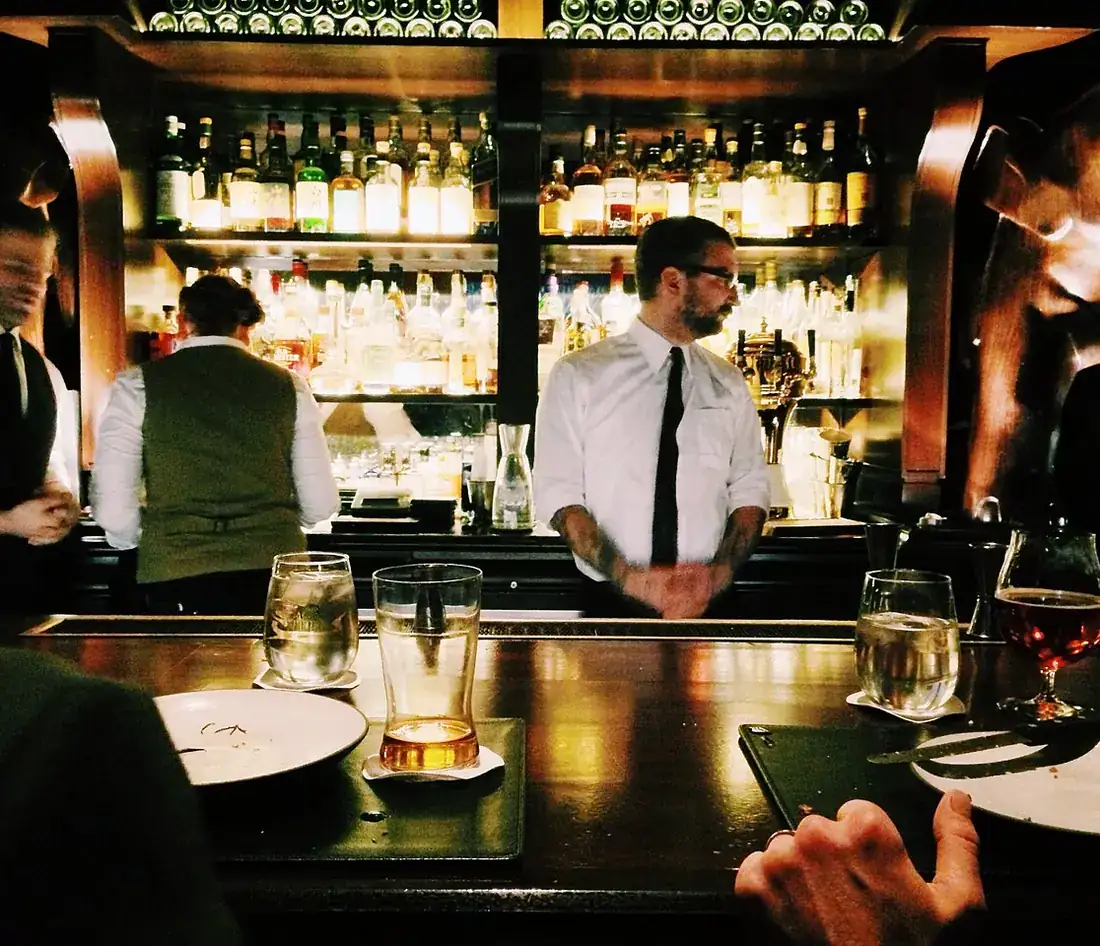 Bartenders in white shirts behind a busy bar
